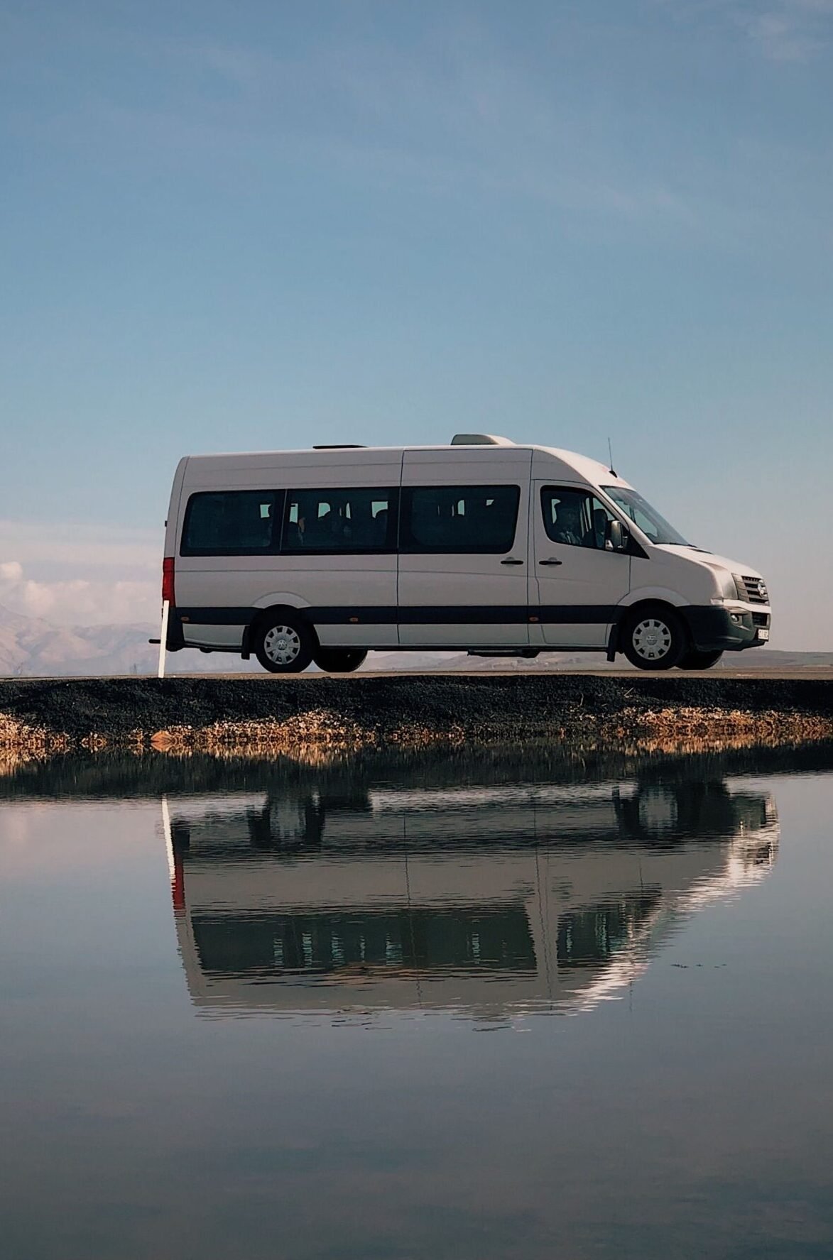 A van and trucks parked by a tranquil lakeshore in Adıyaman, Turkey, beautifully reflected in still water.